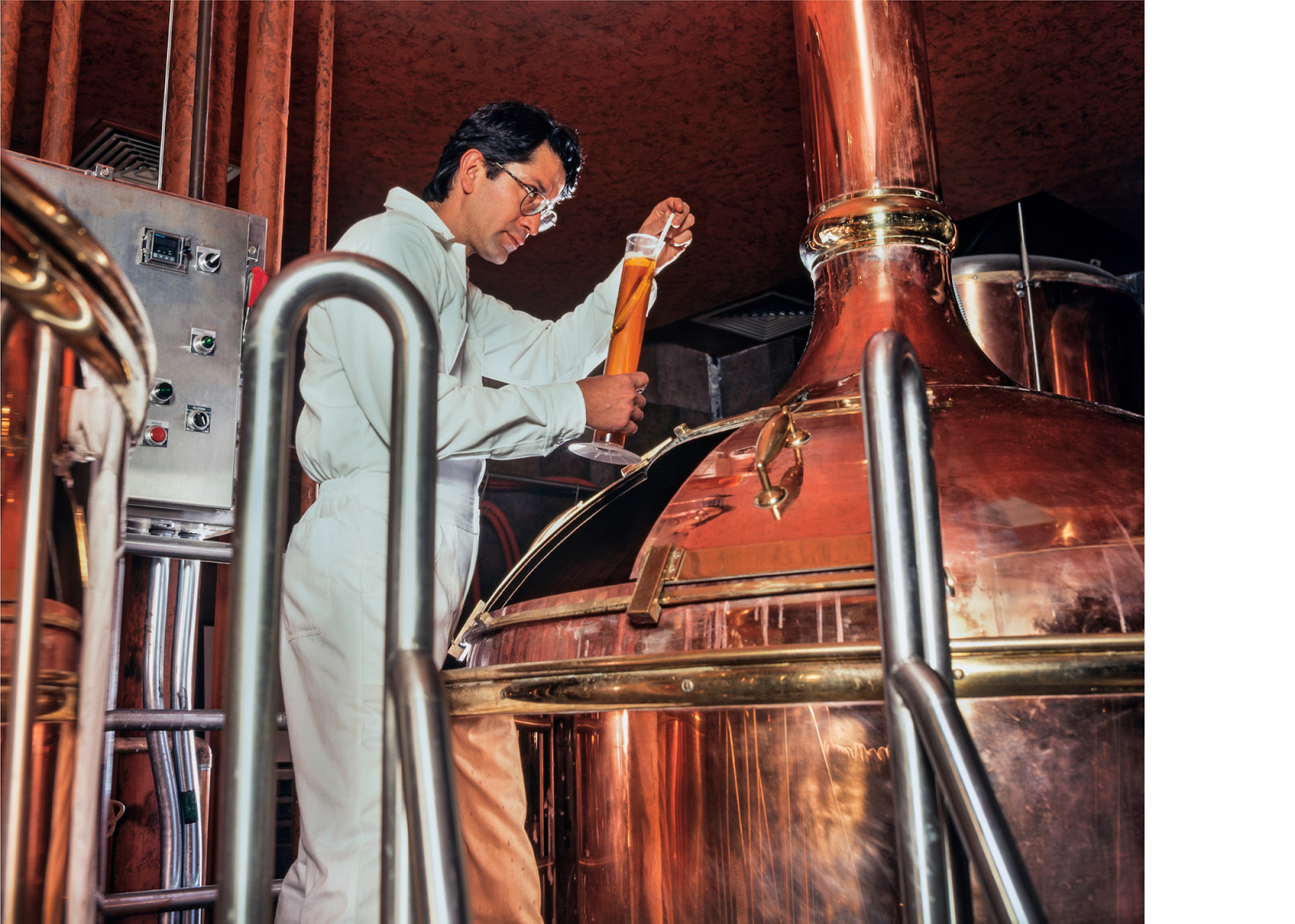 man looking at beaker beside copper beer vessel