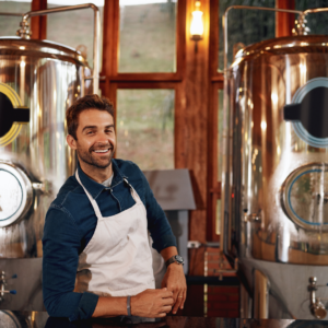man in apron between two vats of beer