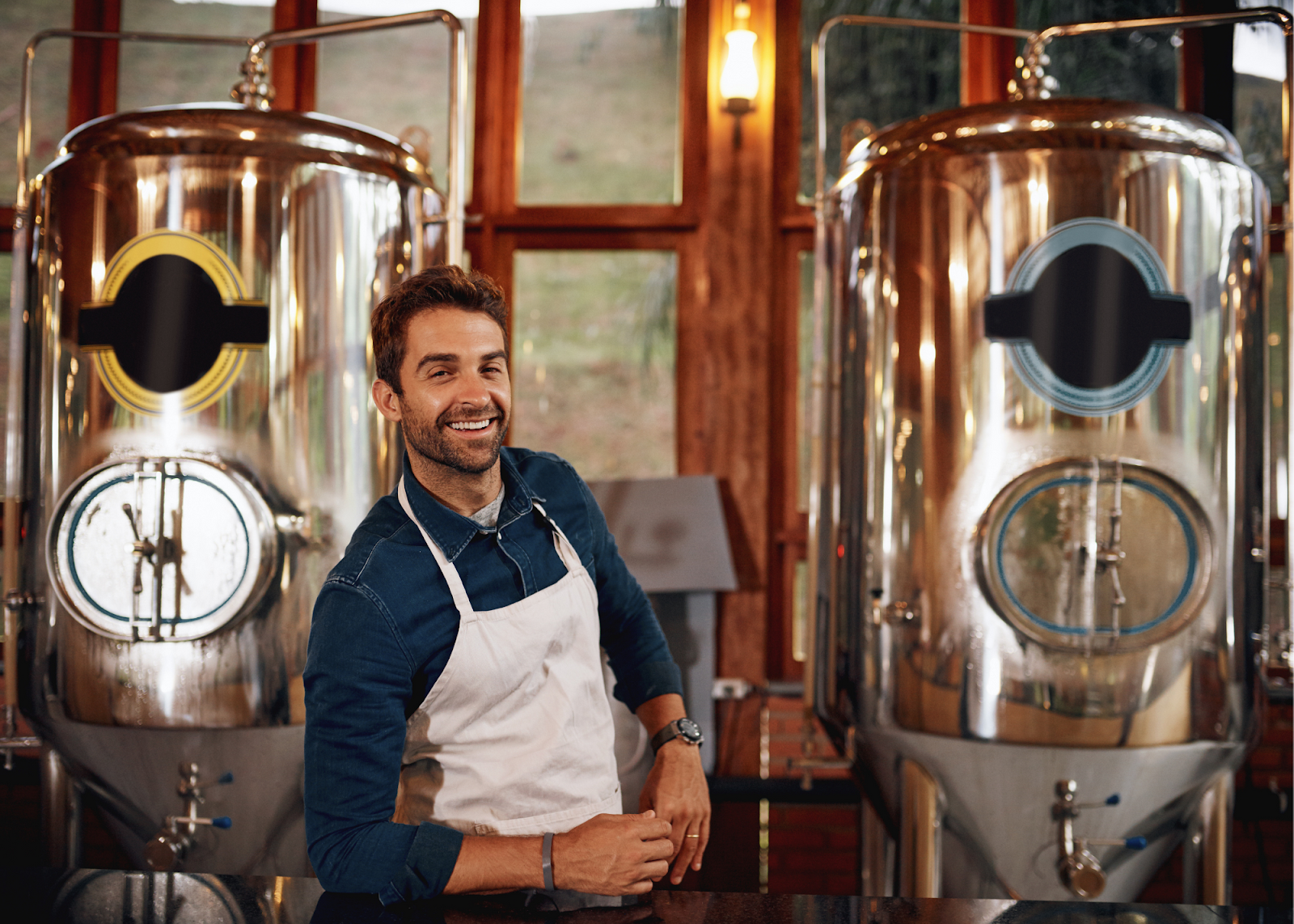 man in apron between two vats of beer